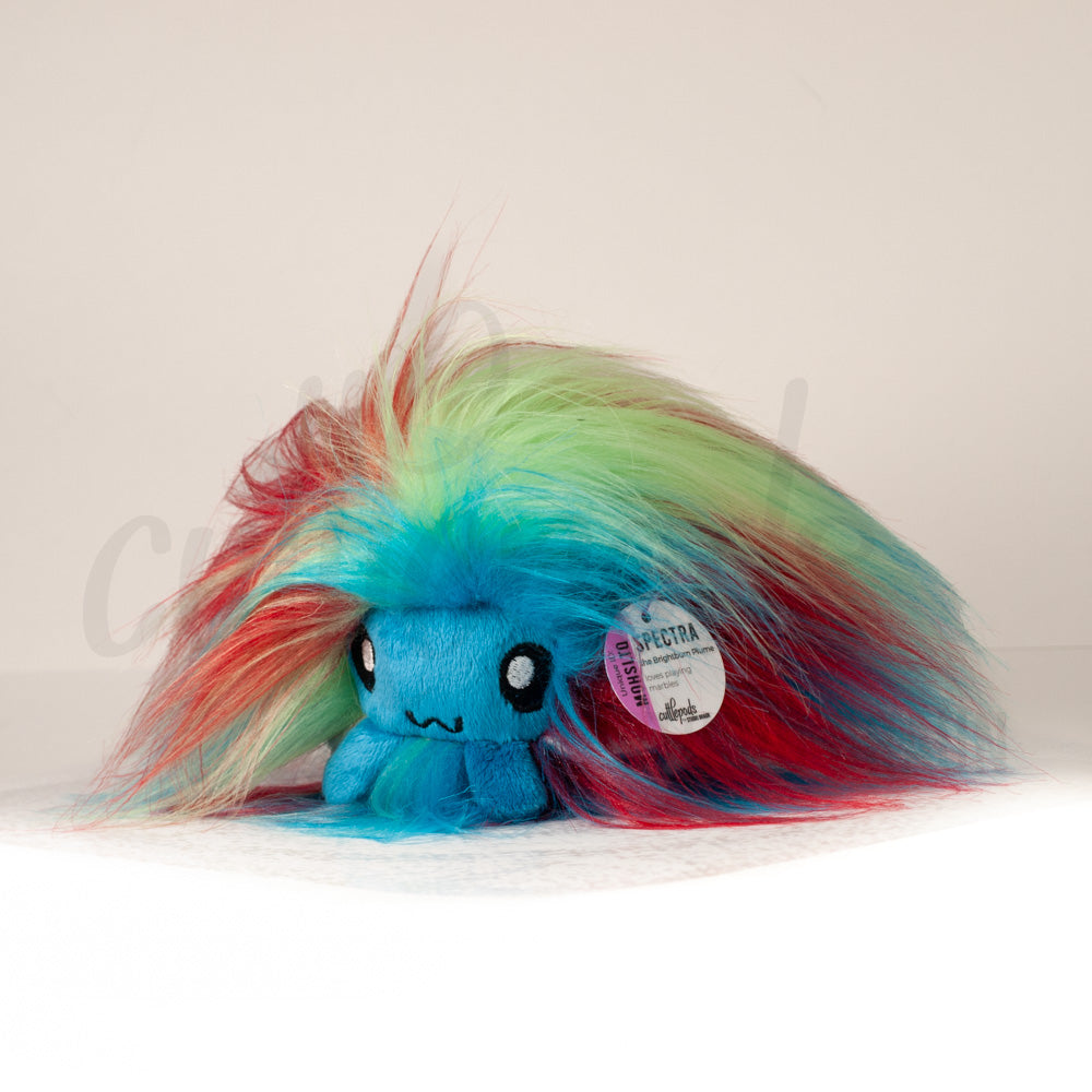 Front view of a cuttlepod plush toy, captured at a slight angle to highlight its charming features: large, cartoonish eyes, ruffled fins, and a cuddly, furry texture.