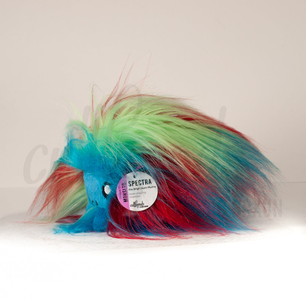 Side profile view of a cuttlepod plush toy, showcasing two-tone ruffled fins, and a cuddly, furry body.