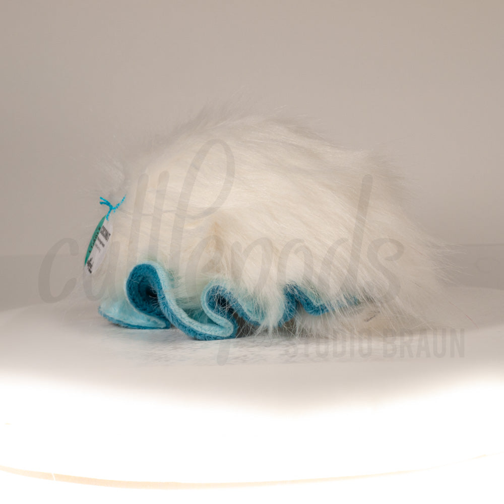 Slightly angled back view of a cuttlepod plush toy, highlighting two-tone ruffled fins, and a cuddly, furry body that comes to a soft point at the rear.