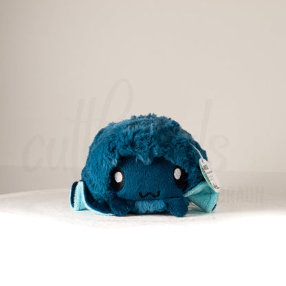 Front view of a cuttlepod plush toy, showcasing its unique form with large, cartoonish eyes, ruffled fins, and a cuddly, furry texture.