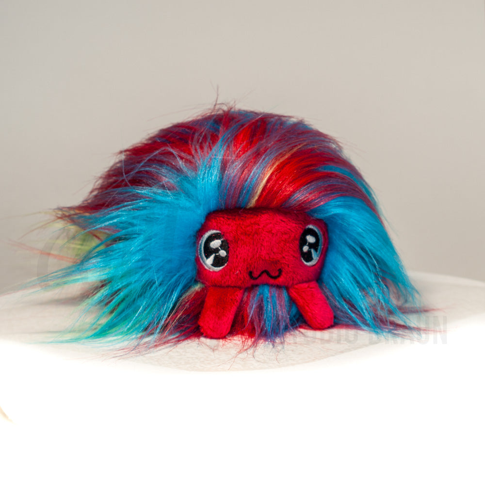 Front view of a cuttlepod plush toy, showcasing its unique form with large, cartoonish eyes, ruffled fins, and a cuddly, furry texture.