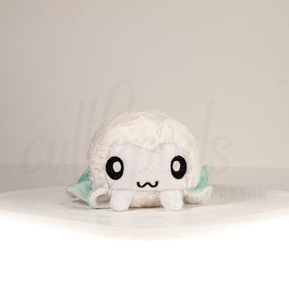 Front view of a cuttlepod plush toy, showcasing its unique form with large, cartoonish eyes, ruffled fins, and a cuddly, furry texture.