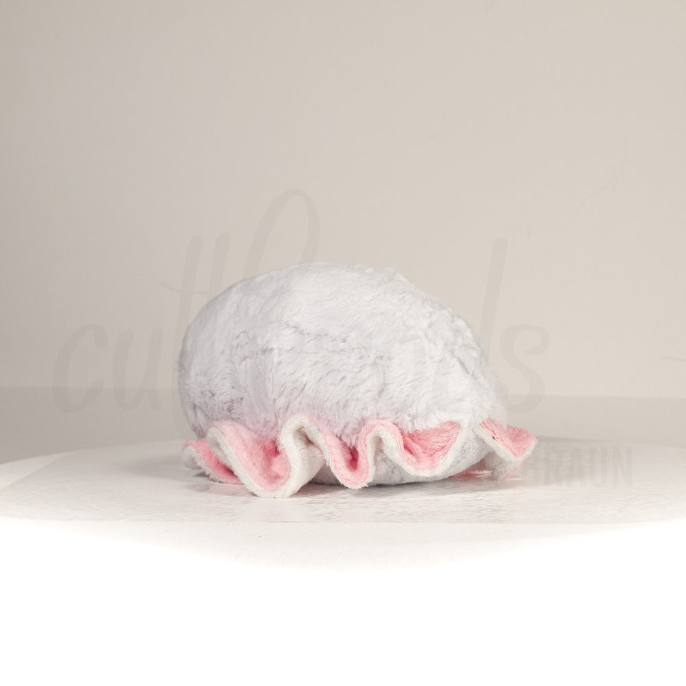 Slightly angled back view of a cuttlepod plush toy, highlighting two-tone ruffled fins, and a cuddly, furry body that comes to a soft point at the rear.