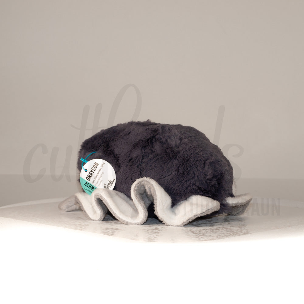 Slightly angled back view of a cuttlepod plush toy, highlighting two-tone ruffled fins, and a cuddly, furry body that comes to a soft point at the rear.