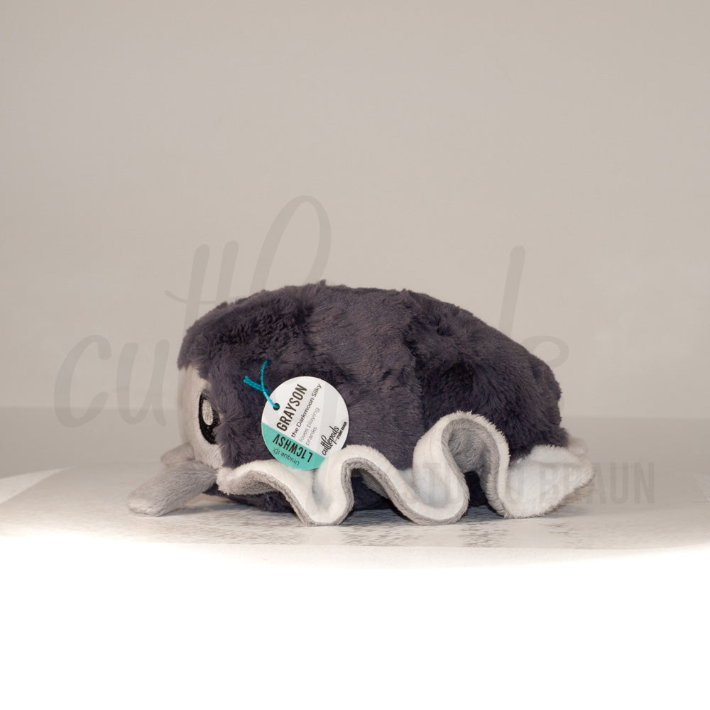 Side profile view of a cuttlepod plush toy, showcasing two-tone ruffled fins, and a cuddly, furry body.