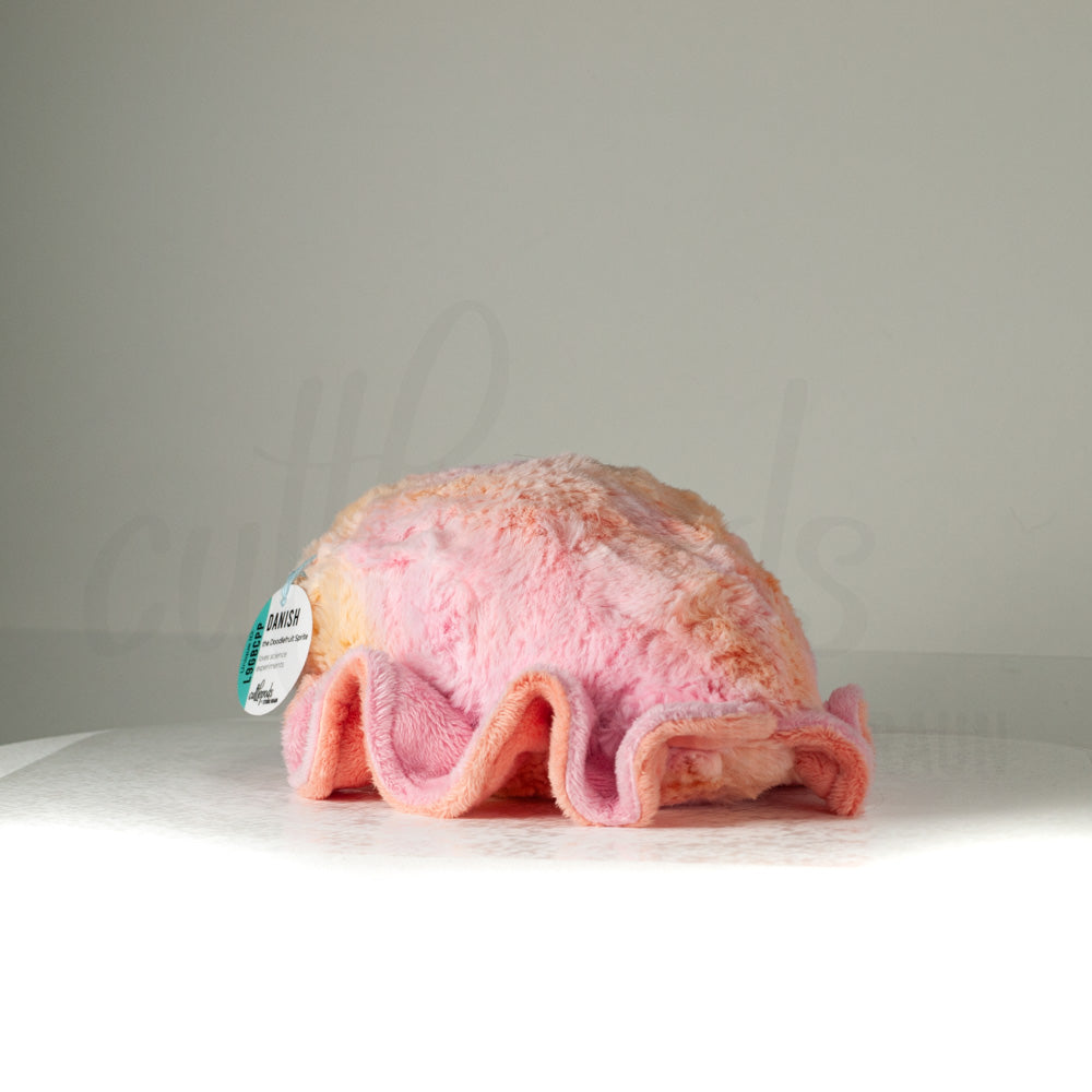 Slightly angled back view of a cuttlepod plush toy, highlighting two-tone ruffled fins, and a cuddly, furry body that comes to a soft point at the rear.