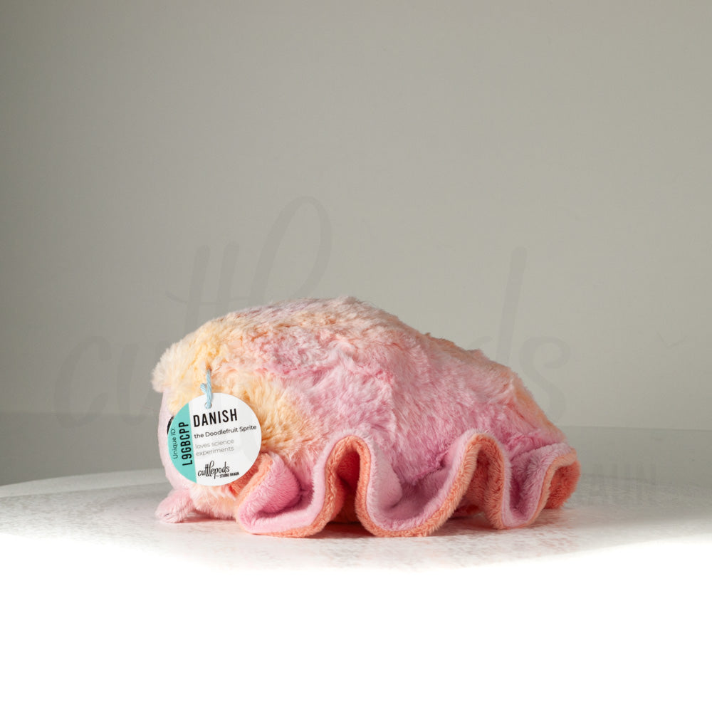 Side profile view of a cuttlepod plush toy, showcasing two-tone ruffled fins, and a cuddly, furry body.