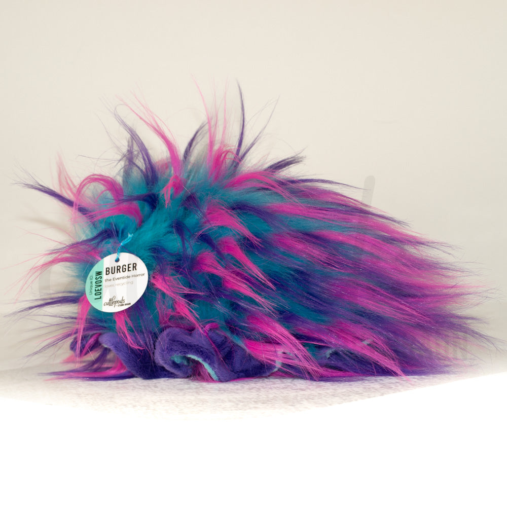 Slightly angled back view of a cuttlepod plush toy, highlighting two-tone ruffled fins, and a cuddly, furry body that comes to a soft point at the rear.