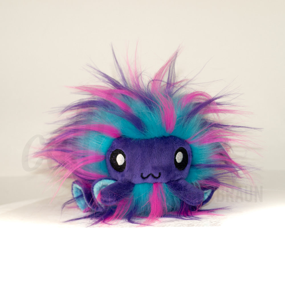 Front view of a cuttlepod plush toy, showcasing its unique form with large, cartoonish eyes, ruffled fins, and a cuddly, furry texture.