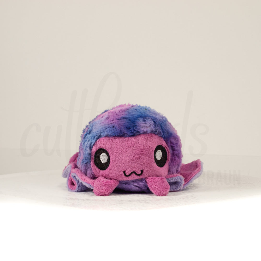 Front view of a cuttlepod plush toy, showcasing its unique form with large, cartoonish eyes, ruffled fins, and a cuddly, furry texture.