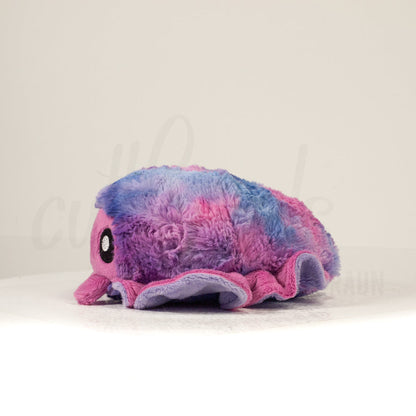 Side profile view of a cuttlepod plush toy, showcasing two-tone ruffled fins, and a cuddly, furry body.