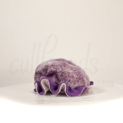 Slightly angled back view of a cuttlepod plush toy, highlighting two-tone ruffled fins, and a cuddly, furry body that comes to a soft point at the rear.