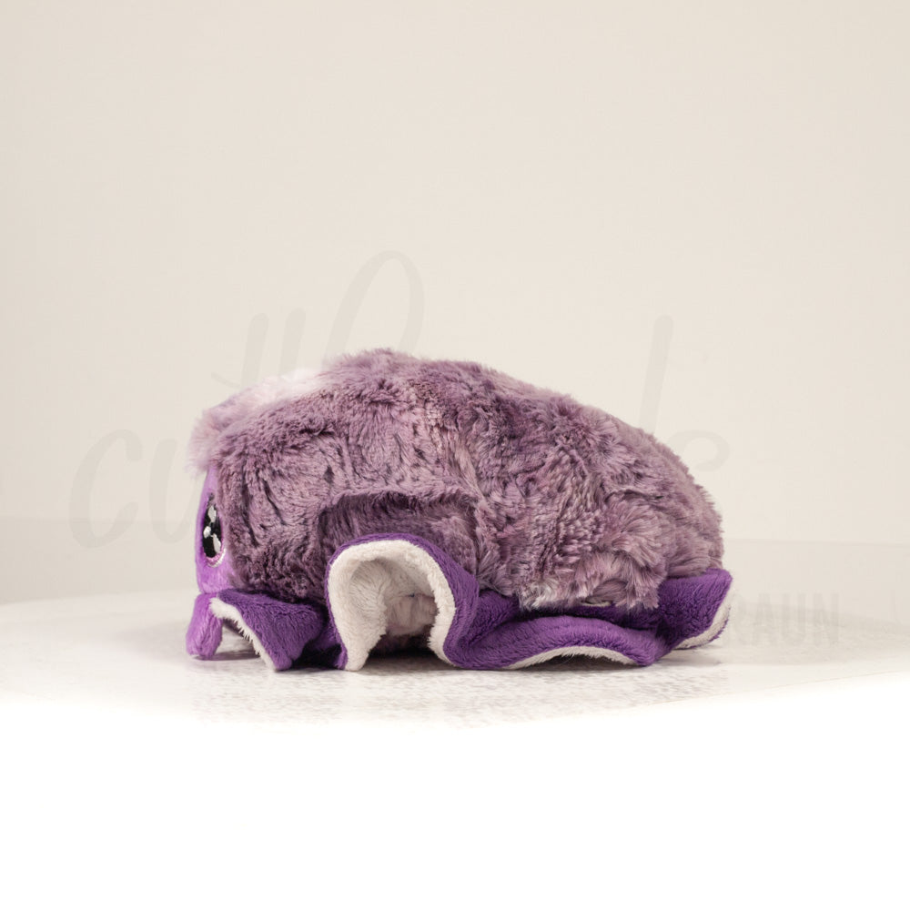 Side profile view of a cuttlepod plush toy, showcasing two-tone ruffled fins, and a cuddly, furry body.