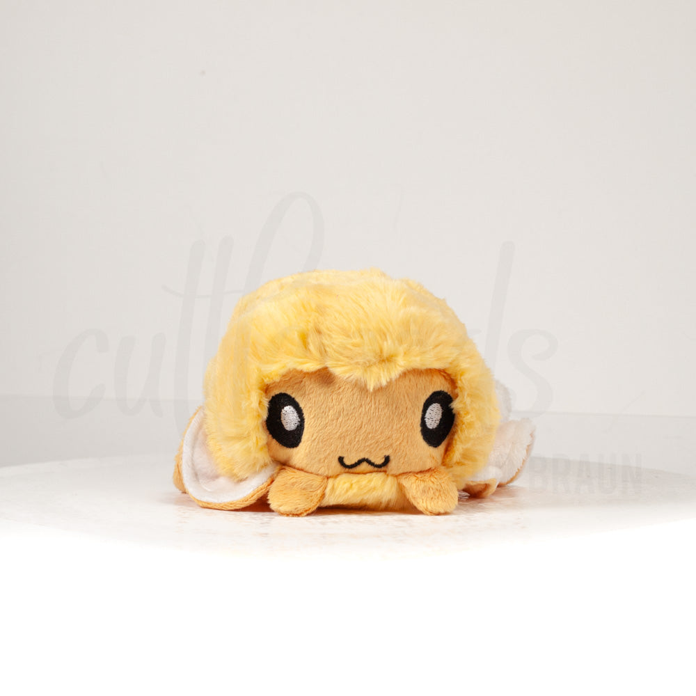 Front view of a cuttlepod plush toy, showcasing its unique form with large, cartoonish eyes, ruffled fins, and a cuddly, furry texture.