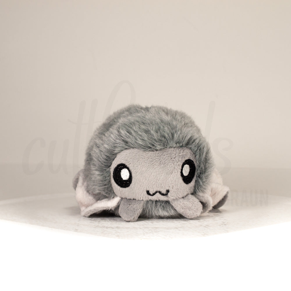 Front view of a cuttlepod plush toy, showcasing its unique form with large, cartoonish eyes, ruffled fins, and a cuddly, furry texture.