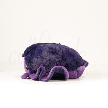 Side profile view of a cuttlepod plush toy, showcasing two-tone ruffled fins, and a cuddly, furry body.