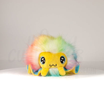 Front view of a cuttlepod plush toy, showcasing its unique form with large, cartoonish eyes, ruffled fins, and a cuddly, furry texture.