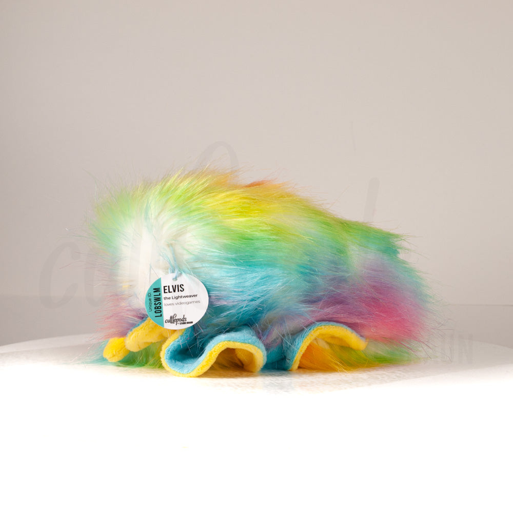 Side profile view of a cuttlepod plush toy, showcasing two-tone ruffled fins, and a cuddly, furry body.