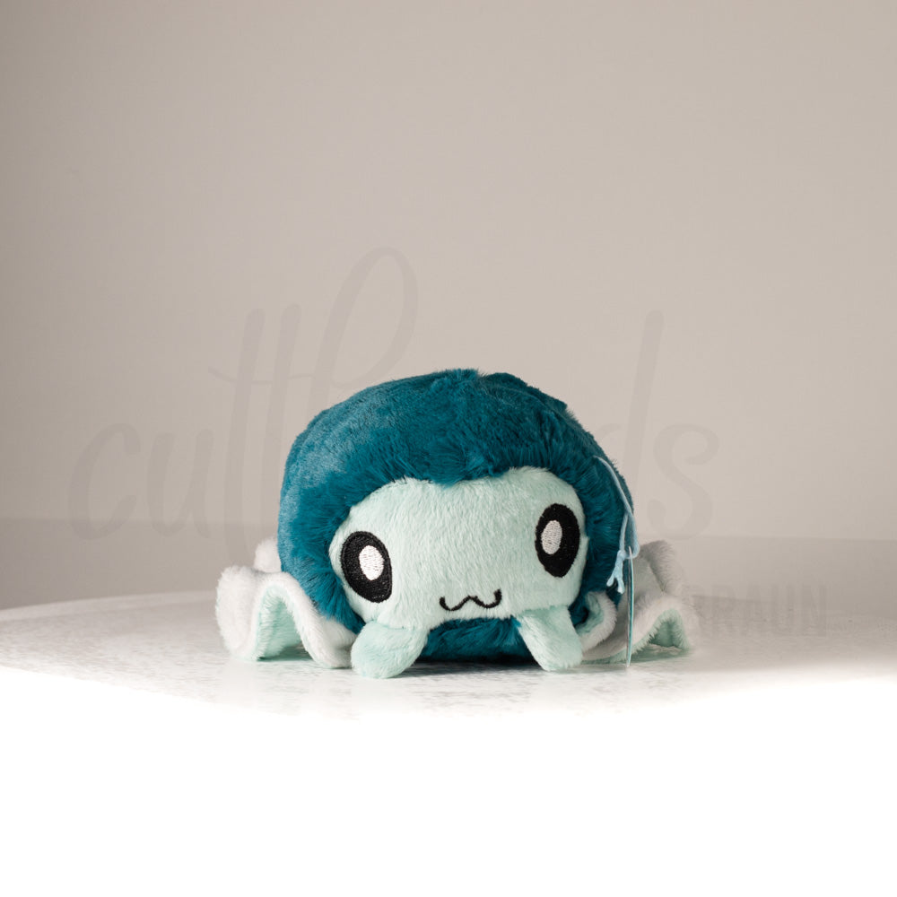 Front view of a cuttlepod plush toy, showcasing its unique form with large, cartoonish eyes, ruffled fins, and a cuddly, furry texture.