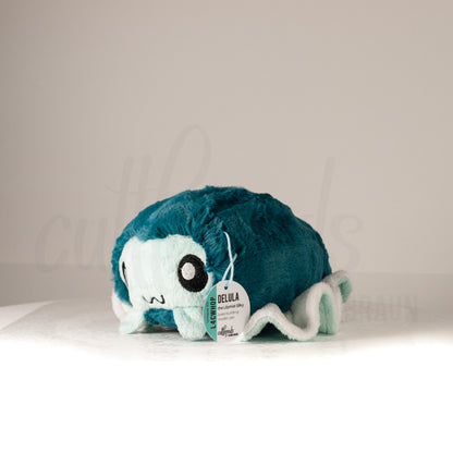 Front view of a cuttlepod plush toy, captured at a slight angle to highlight its charming features: large, cartoonish eyes, ruffled fins, and a cuddly, furry texture.