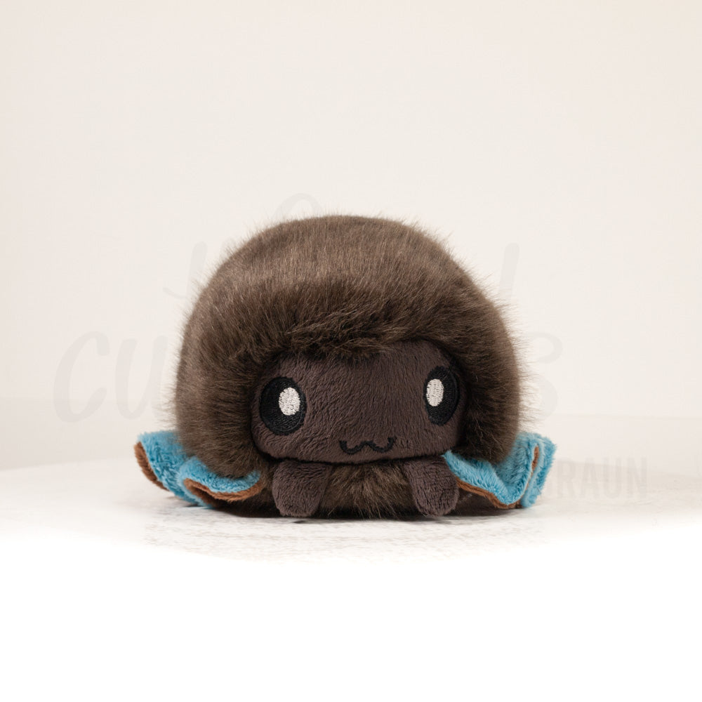 Front view of a cuttlepod plush toy, showcasing its unique form with large, cartoonish eyes, ruffled fins, and a cuddly, furry texture.