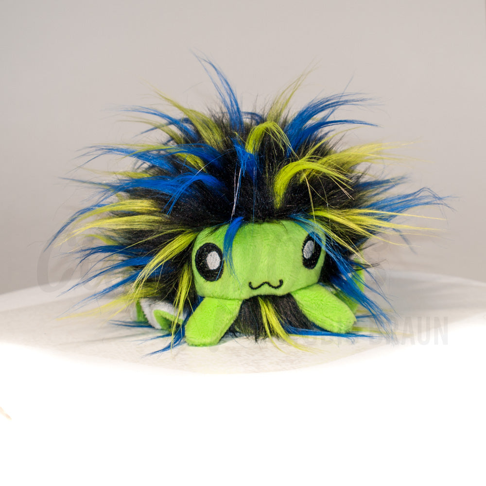 Front view of a cuttlepod plush toy, showcasing its unique form with large, cartoonish eyes, ruffled fins, and a cuddly, furry texture.