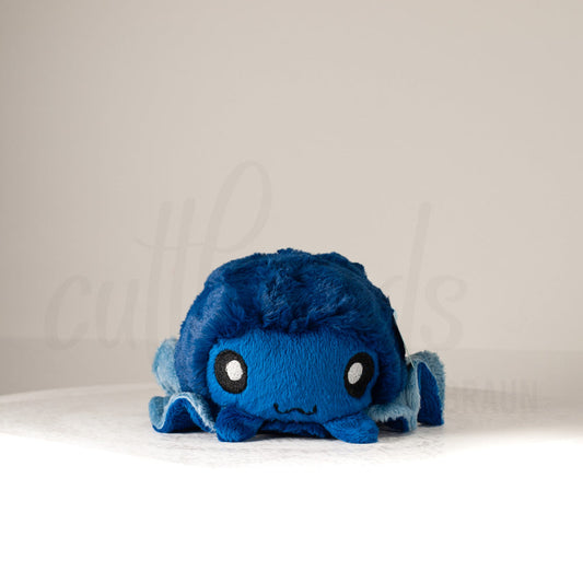 Front view of a cuttlepod plush toy, showcasing its unique form with large, cartoonish eyes, ruffled fins, and a cuddly, furry texture.