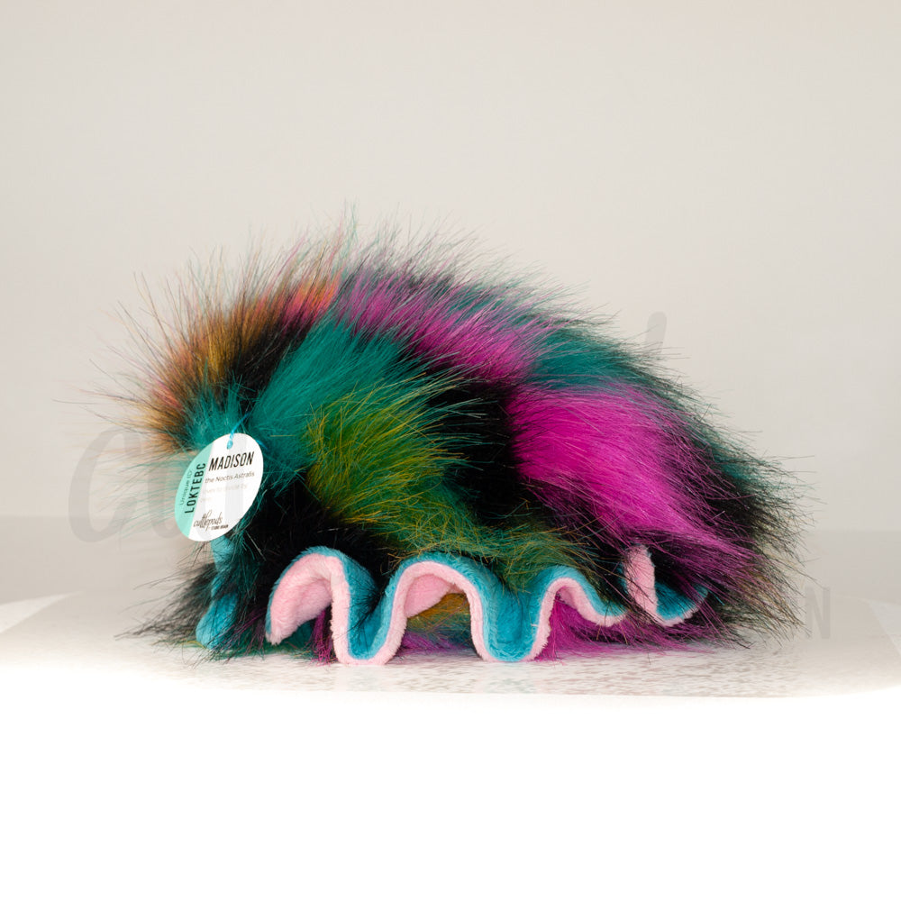 Side profile view of a cuttlepod plush toy, showcasing two-tone ruffled fins, and a cuddly, furry body.