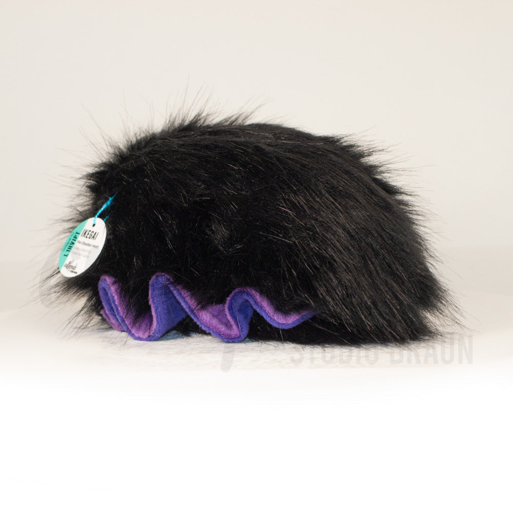 Slightly angled back view of a cuttlepod plush toy, highlighting two-tone ruffled fins, and a cuddly, furry body that comes to a soft point at the rear.