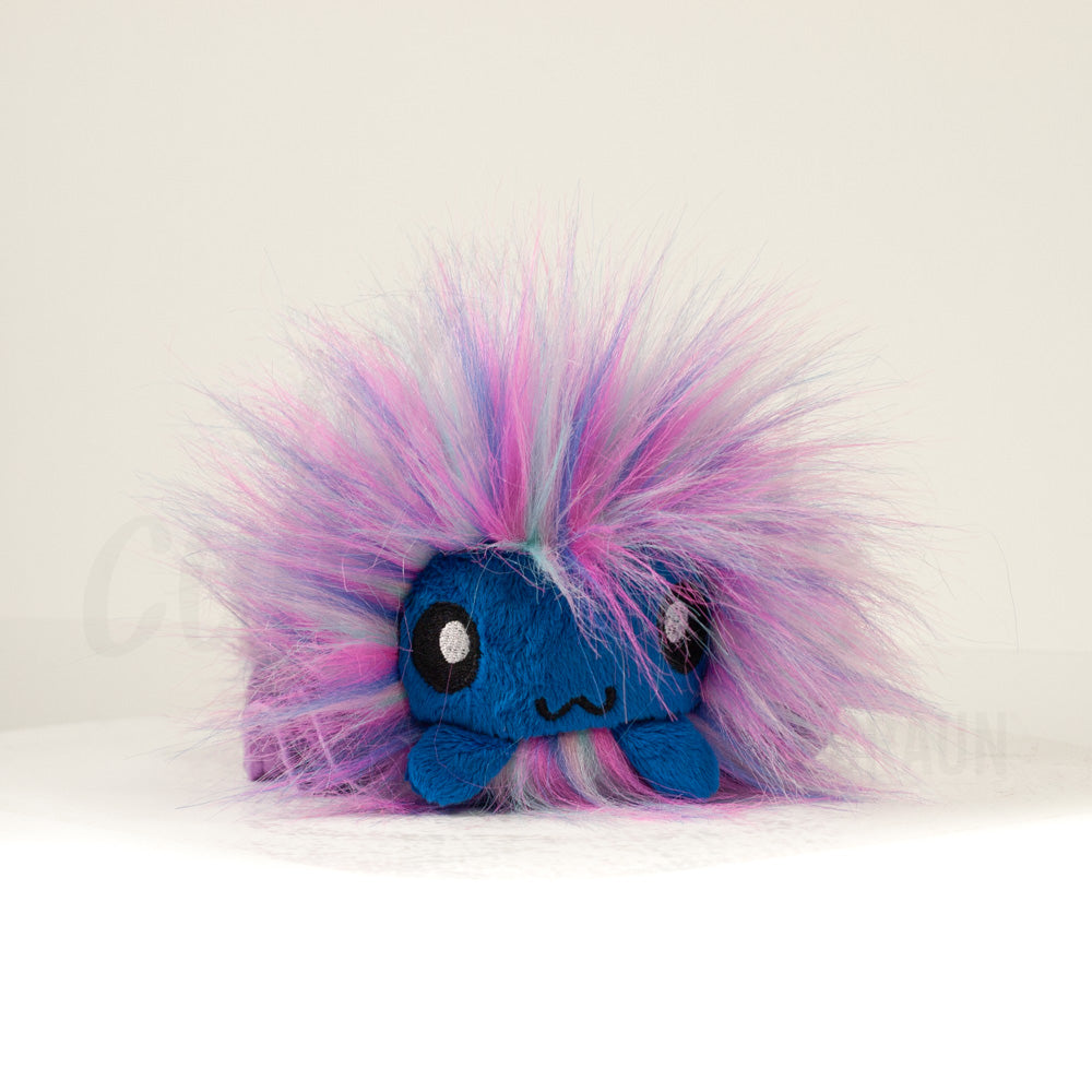 Front view of a cuttlepod plush toy, showcasing its unique form with large, cartoonish eyes, ruffled fins, and a cuddly, furry texture.