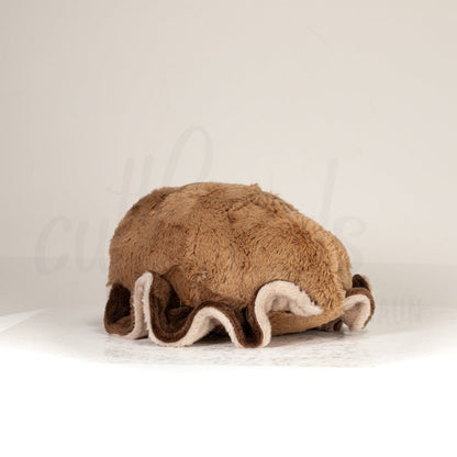 Slightly angled back view of a cuttlepod plush toy, highlighting two-tone ruffled fins, and a cuddly, furry body that comes to a soft point at the rear.