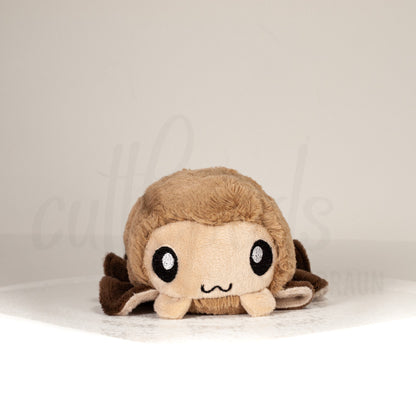 Front view of a cuttlepod plush toy, showcasing its unique form with large, cartoonish eyes, ruffled fins, and a cuddly, furry texture.