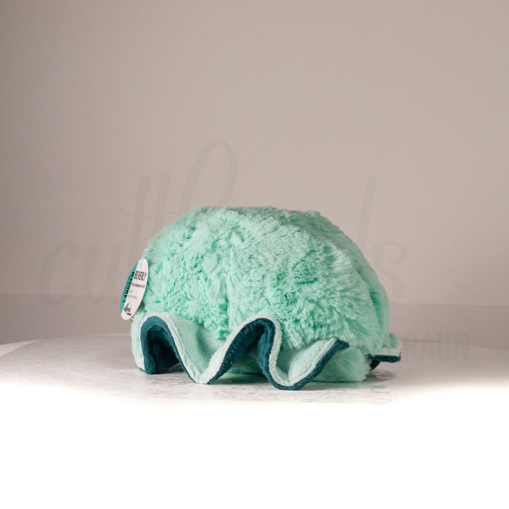 Slightly angled back view of a cuttlepod plush toy, highlighting two-tone ruffled fins, and a cuddly, furry body that comes to a soft point at the rear.