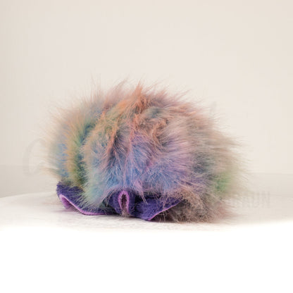 Slightly angled back view of a cuttlepod plush toy, highlighting two-tone ruffled fins, and a cuddly, furry body that comes to a soft point at the rear.