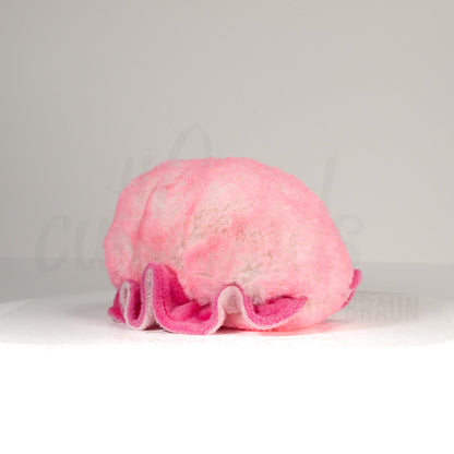 Slightly angled back view of a cuttlepod plush toy, highlighting two-tone ruffled fins, and a cuddly, furry body that comes to a soft point at the rear.