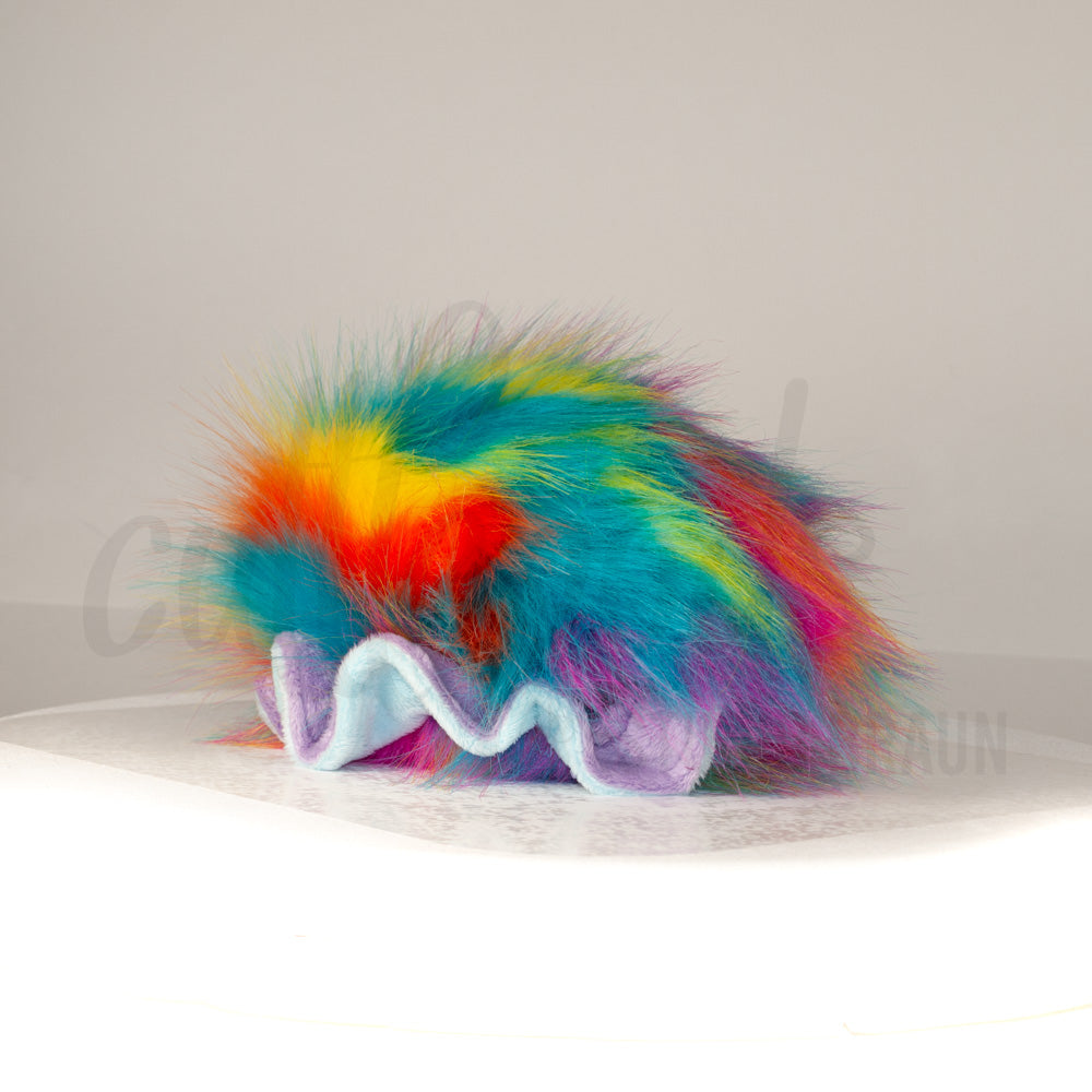 Slightly angled back view of a cuttlepod plush toy, highlighting two-tone ruffled fins, and a cuddly, furry body that comes to a soft point at the rear.