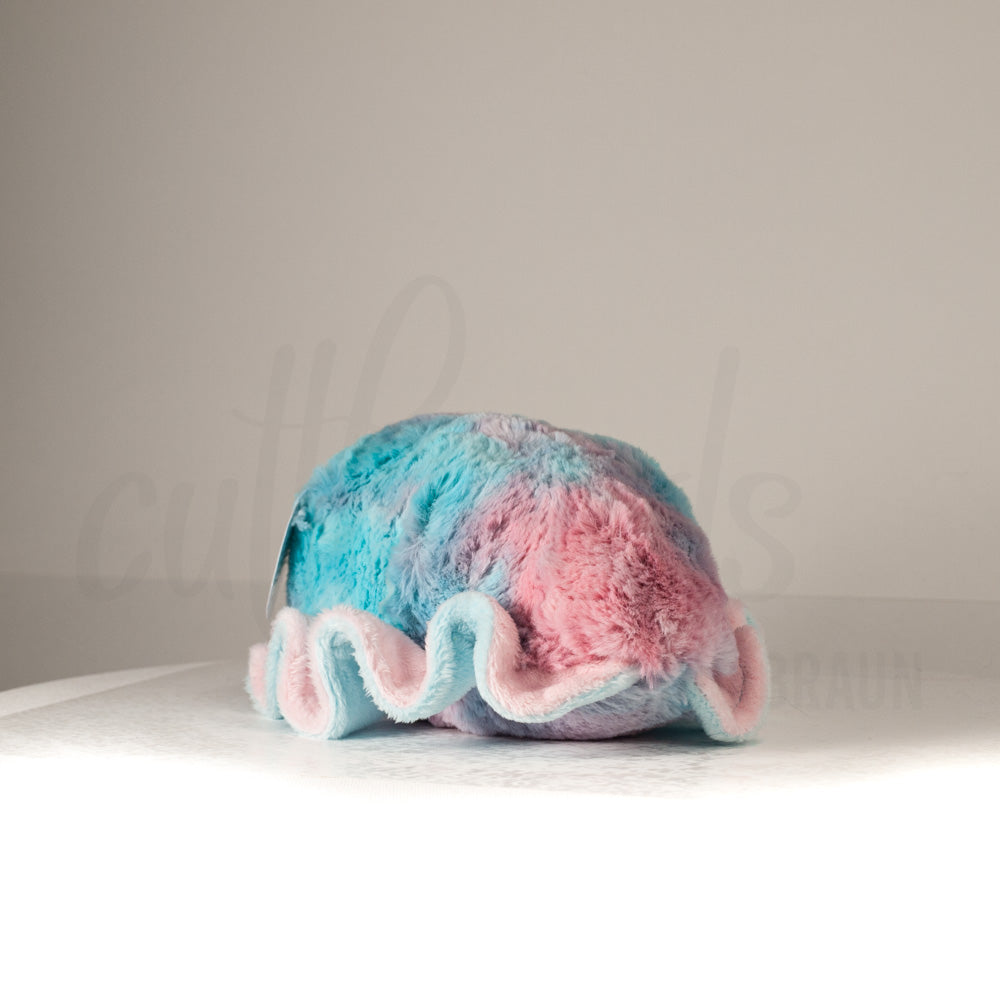 Slightly angled back view of a cuttlepod plush toy, highlighting two-tone ruffled fins, and a cuddly, furry body that comes to a soft point at the rear.