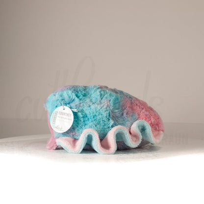 Side profile view of a cuttlepod plush toy, showcasing two-tone ruffled fins, and a cuddly, furry body.