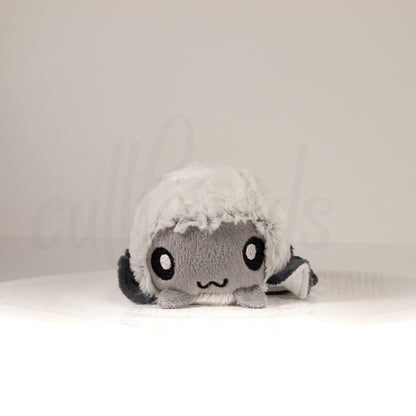 Front view of a cuttlepod plush toy, showcasing its unique form with large, cartoonish eyes, ruffled fins, and a cuddly, furry texture.