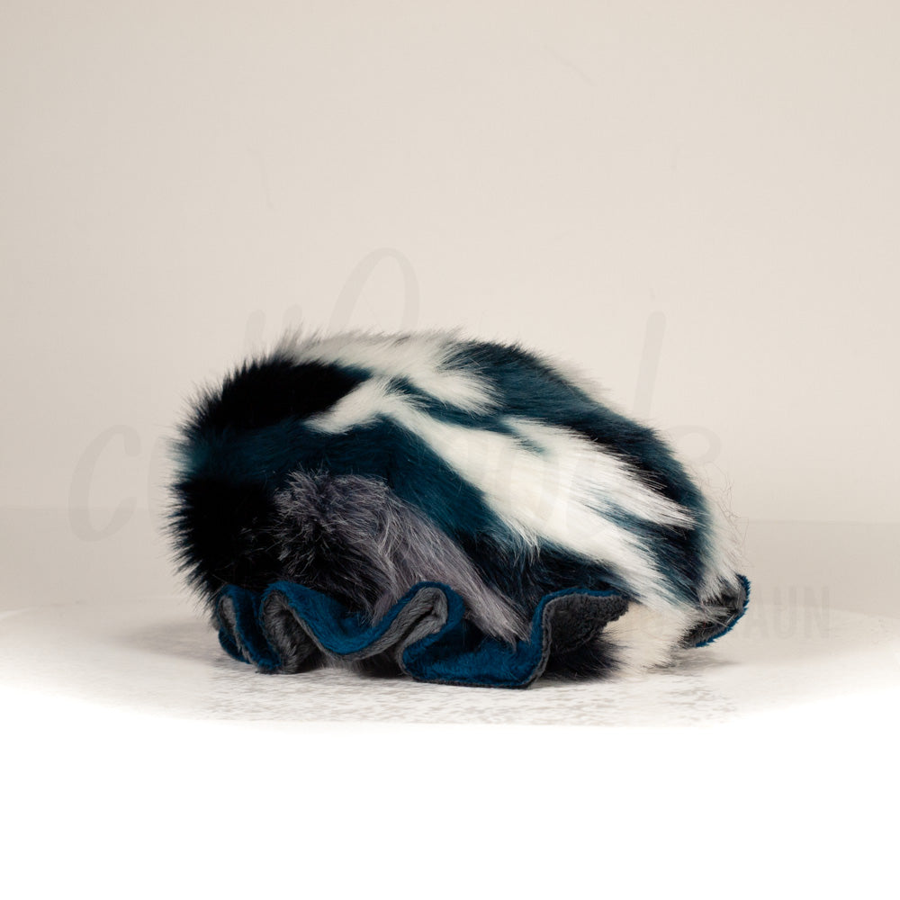 Slightly angled back view of a cuttlepod plush toy, highlighting two-tone ruffled fins, and a cuddly, furry body that comes to a soft point at the rear.