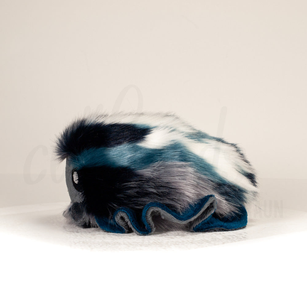 Side profile view of a cuttlepod plush toy, showcasing two-tone ruffled fins, and a cuddly, furry body.