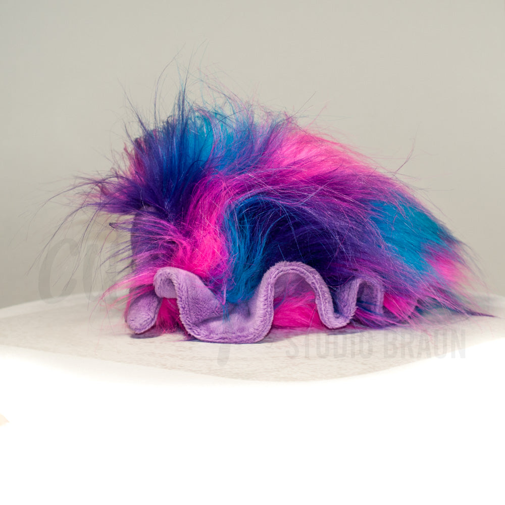 Slightly angled back view of a cuttlepod plush toy, highlighting two-tone ruffled fins, and a cuddly, furry body that comes to a soft point at the rear.