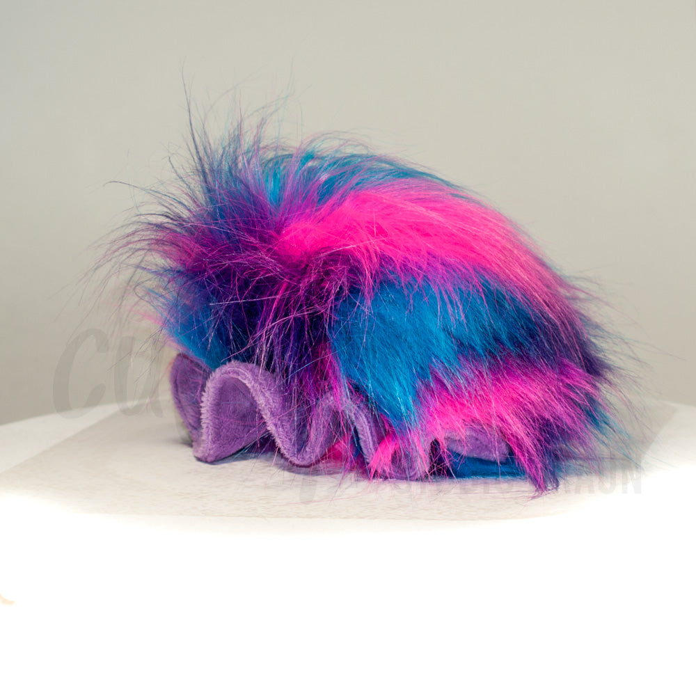 Slightly angled back view of a cuttlepod plush toy, highlighting two-tone ruffled fins, and a cuddly, furry body that comes to a soft point at the rear.