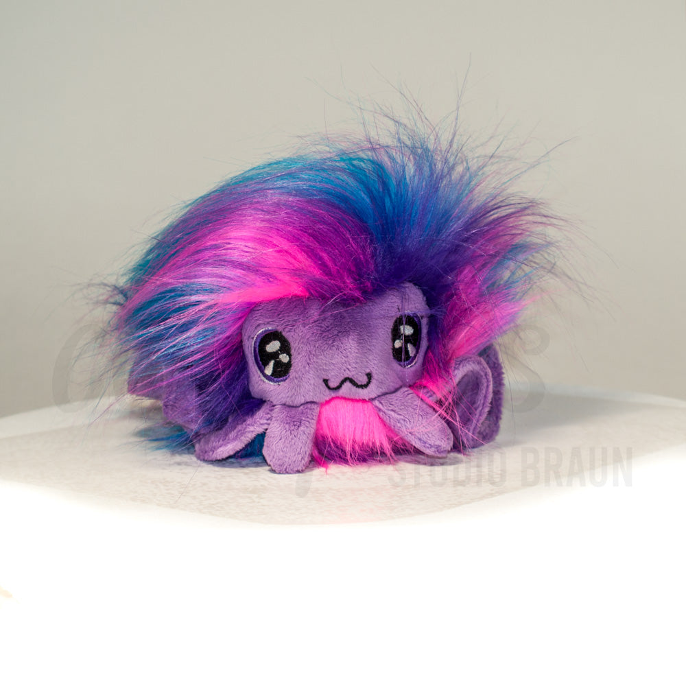 Front view of a cuttlepod plush toy, showcasing its unique form with large, cartoonish eyes, ruffled fins, and a cuddly, furry texture.