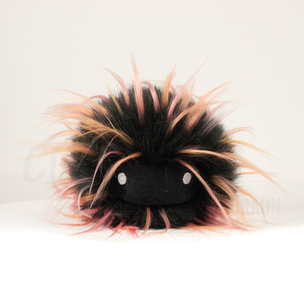 Front view of a cuttlepod plush toy, showcasing its unique form with large, cartoonish eyes, ruffled fins, and a cuddly, furry texture.