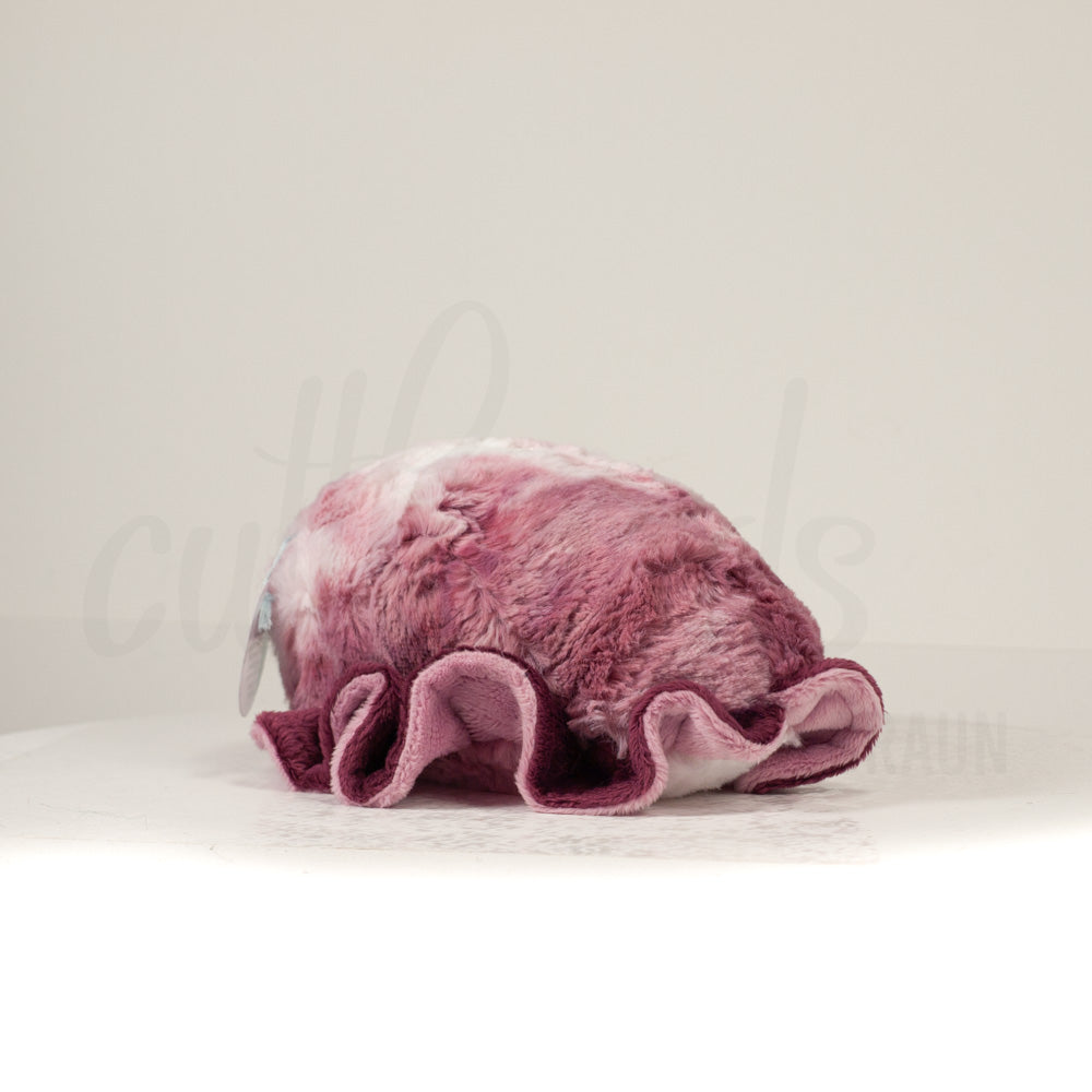 Slightly angled back view of a cuttlepod plush toy, highlighting two-tone ruffled fins, and a cuddly, furry body that comes to a soft point at the rear.