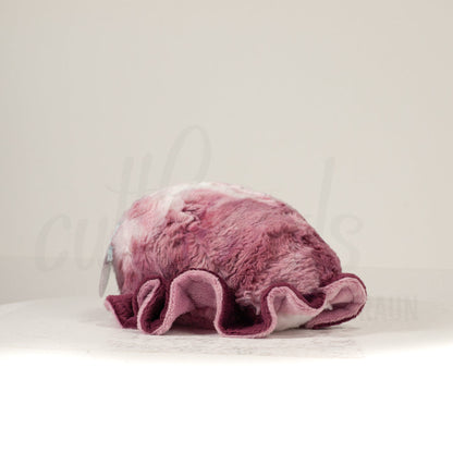 Slightly angled back view of a cuttlepod plush toy, highlighting two-tone ruffled fins, and a cuddly, furry body that comes to a soft point at the rear.