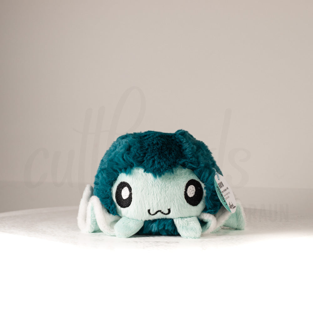 Front view of a cuttlepod plush toy, showcasing its unique form with large, cartoonish eyes, ruffled fins, and a cuddly, furry texture.