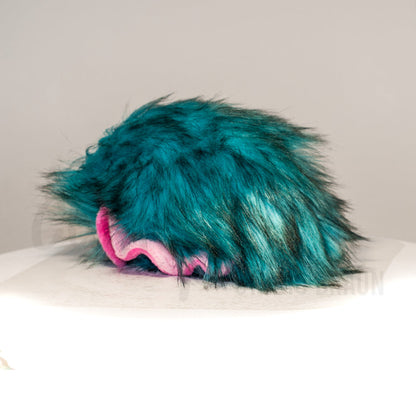 Slightly angled back view of a cuttlepod plush toy, highlighting two-tone ruffled fins, and a cuddly, furry body that comes to a soft point at the rear.