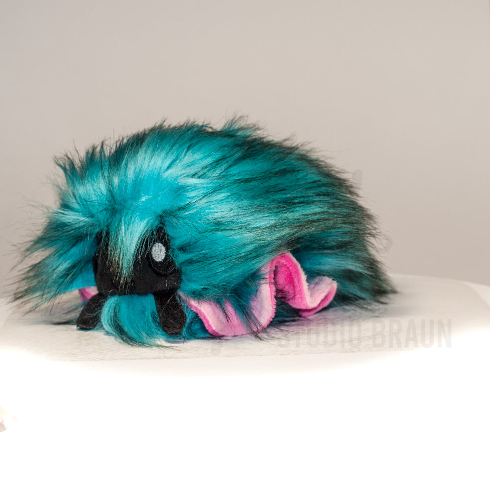 Front view of a cuttlepod plush toy, captured at a slight angle to highlight its charming features: large, cartoonish eyes, ruffled fins, and a cuddly, furry texture.